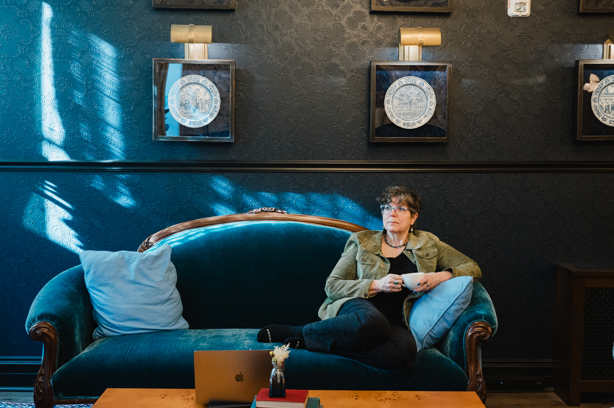 Picture of Barb seated on a comfy couch with a cup of tea in a beautiful room, sunlight streaming in