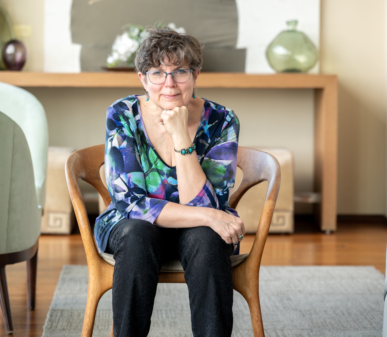 Barb Nangle seated confidently in a multi colored shirt with a pleasant smile on her face