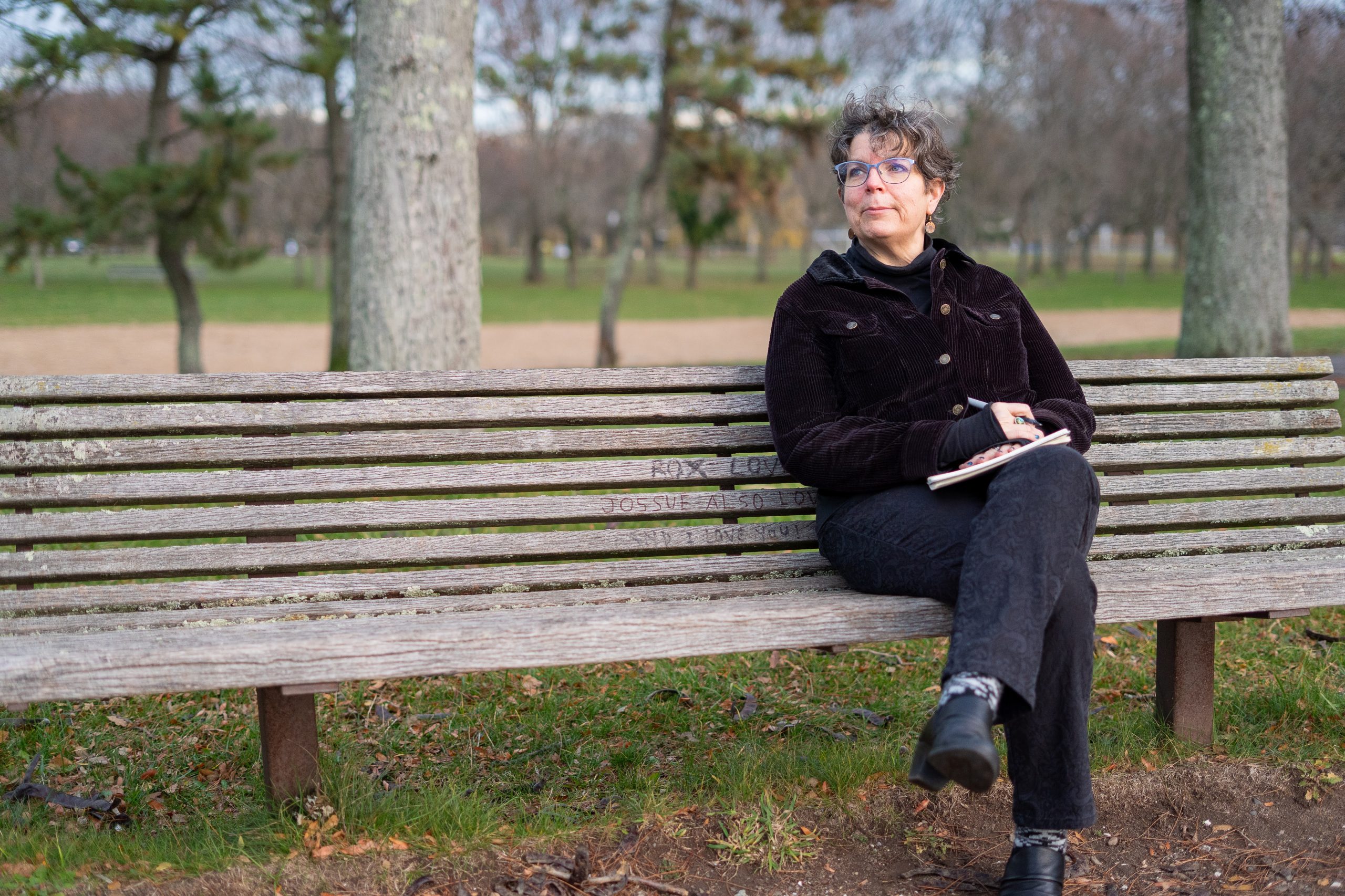 Barb sitting on a park bench with a journal on her lap, looking up and off to the side
