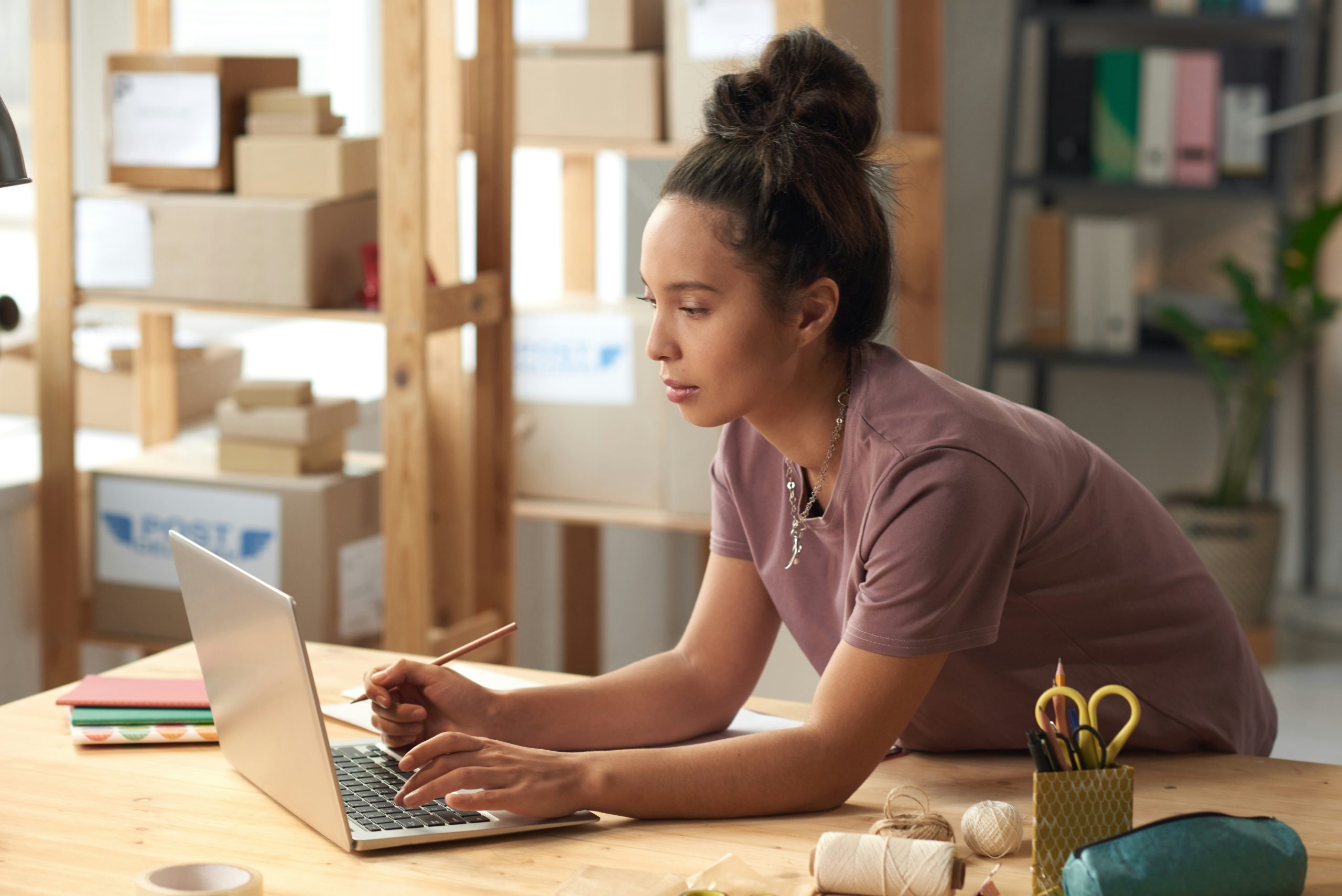 Women leaning over her work table and working on her laptop